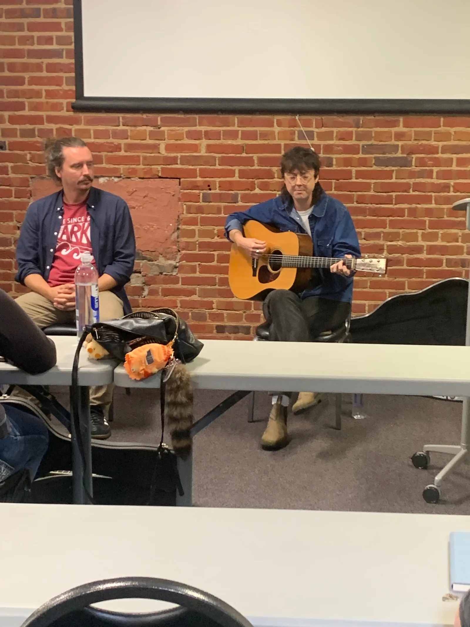 An individual listening to another play a guitar